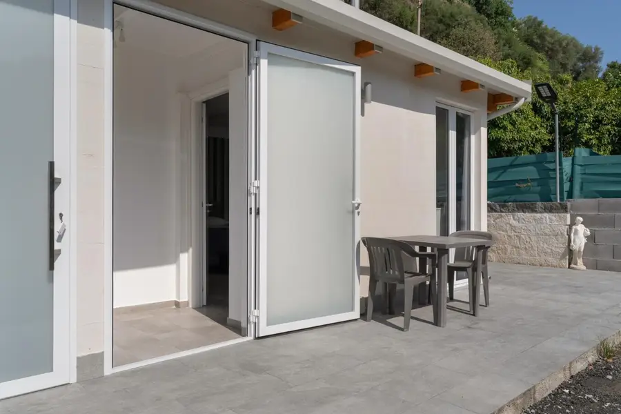 Patio davanti al bungalow con tavolo e sedie, porta-finestra aperta sulla camera